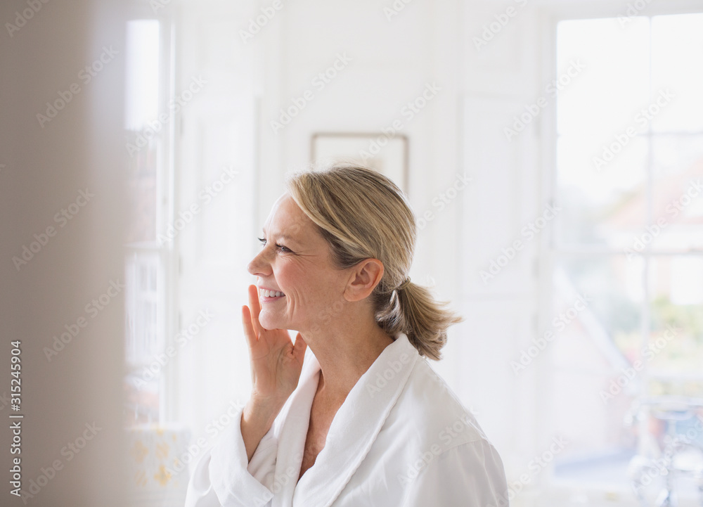Smiling mature woman applying moisturizer to face in bathroom Smiling mature woman applying moisturizer to face in bathroom