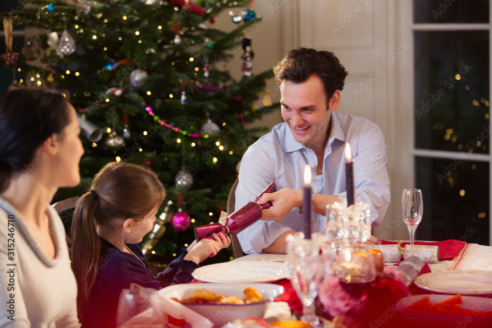 Father and daughter pulling Christmas cracker at candlelight dinner table Father and daughter pulling Christmas cracker at candlelight dinner table