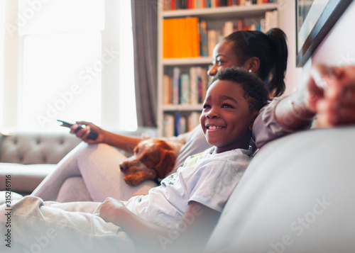 Happy boy watching TV with mother and dog on living room sofa