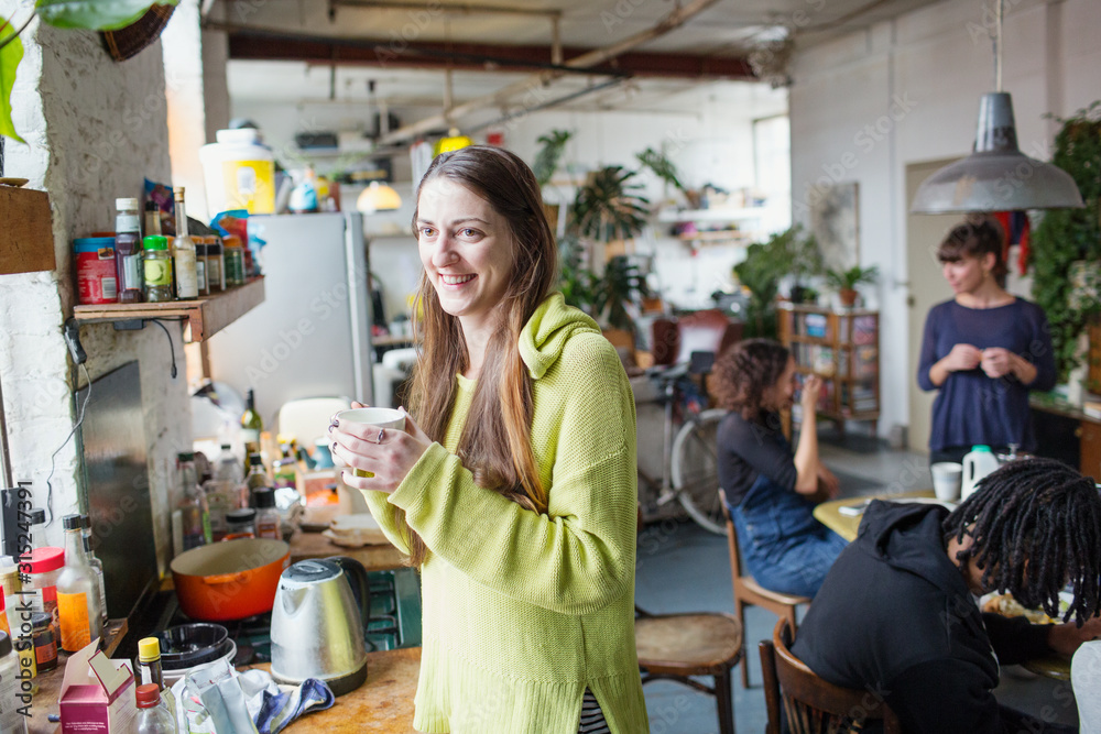 Smiling young woman drinking coffee with roommates in apartment kitchen Smiling young woman drinking coffee with roommates in apartment kitchen