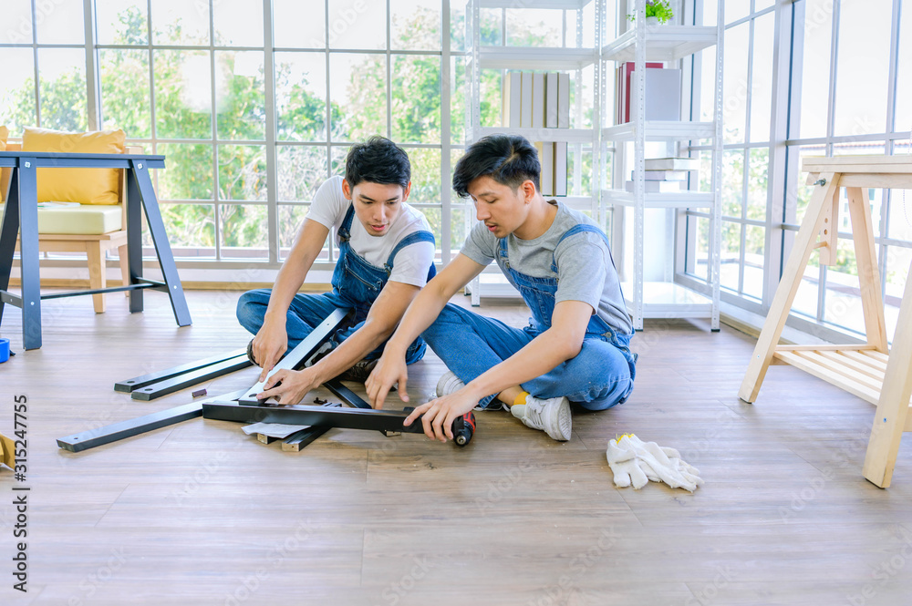 Fototapeta premium profession, carpentry, woodwork and people concept - two carpenters with electric drill drilling wood plank at workshop.