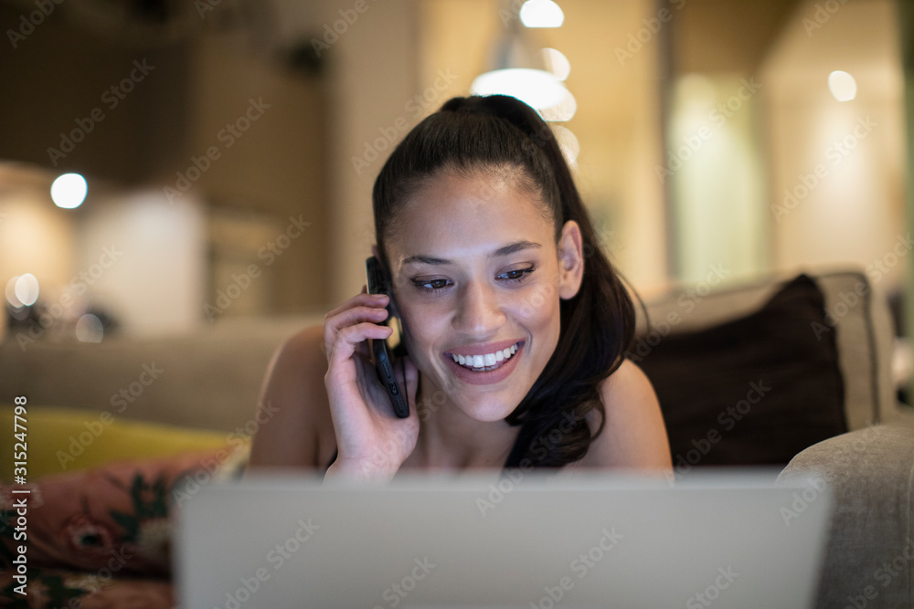 Smiling woman talking on smart phone at laptop on sofa Smiling woman talking on smart phone at laptop on sofa