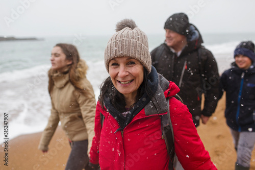 Portrait smiling woman in warm clothing with family on snowy winter ocean beach photo