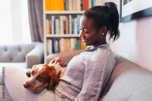Young woman cuddling with dog on living room sofa