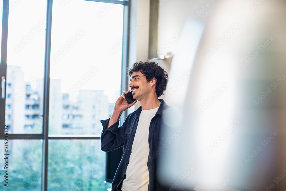 Smiling man talking on smart phone at urban apartment window Smiling man talking on smart phone at urban apartment window