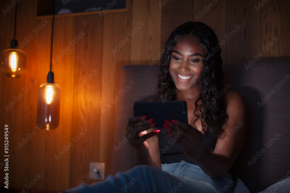 Smiling young woman using smart phone in dark bedroom Smiling young woman using smart phone in dark bedroom