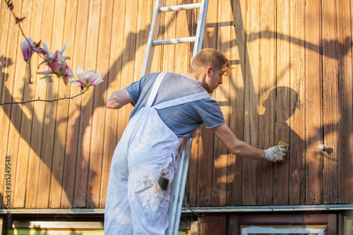 Male worker on ladder staining wood siding on home exterior