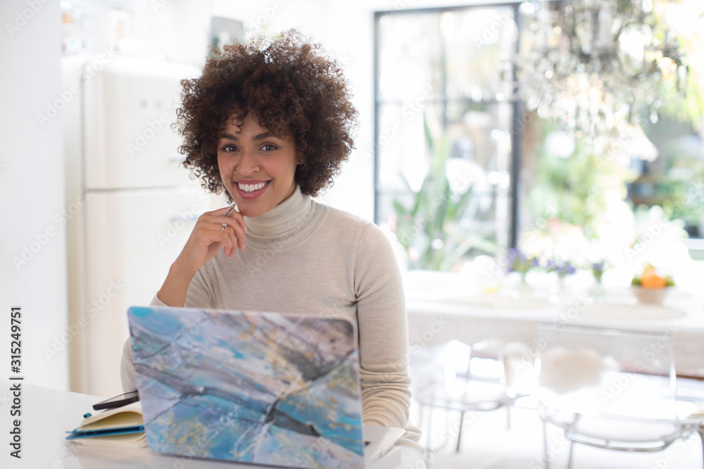 © Sam Edwards/Caia Image - Portrait happy young woman working at laptop in kitchen