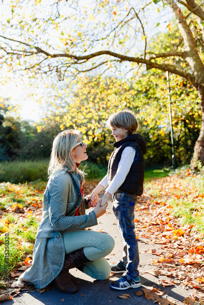Mother and son holding hands and talking in sunny autumn park Mother and son holding hands and talking in sunny autumn park