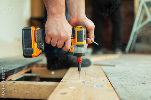 Close up construction worker using power drill installing floorboard photo