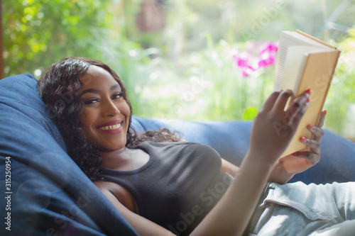 Portrait happy young woman relaxing reading book in beanbag chair