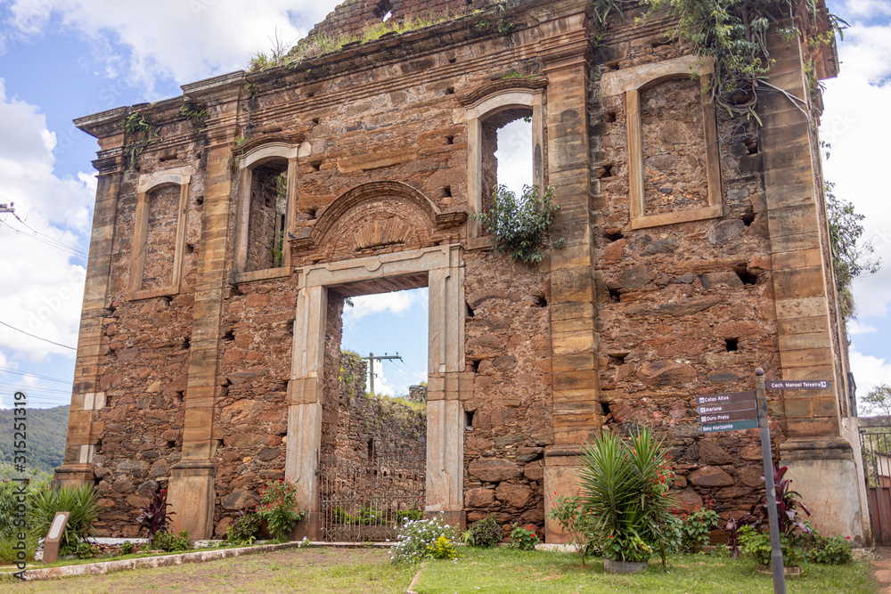 Ruins of the Church of Our Lady of the Conception of Lapa with only the overgrown facade and exterior standing you can look through against a blue sky with clouds