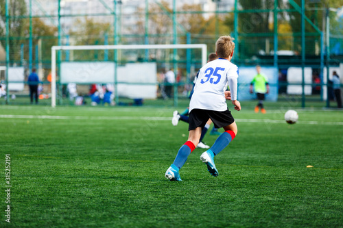 Boys in white and blue sportswear plays football on field, dribbles ball. Young soccer players with ball on green grass. Training, football, active lifestyle for kids concept © Natali