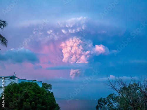 Taal Volcano eruption at sunset, its plume visible in the sky over the lights of Batangas City, viewed from Mindoro Island, 30 miles away, on Jan 12, 2020. photo