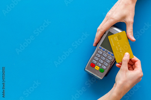 Contactless payment, paypass. Hand hold bank card near terminal on blue background top-down copy space photo