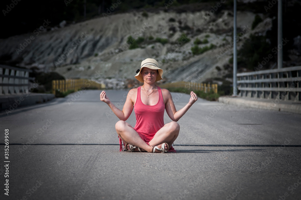 girl in a pink dress meditates sitting on the road