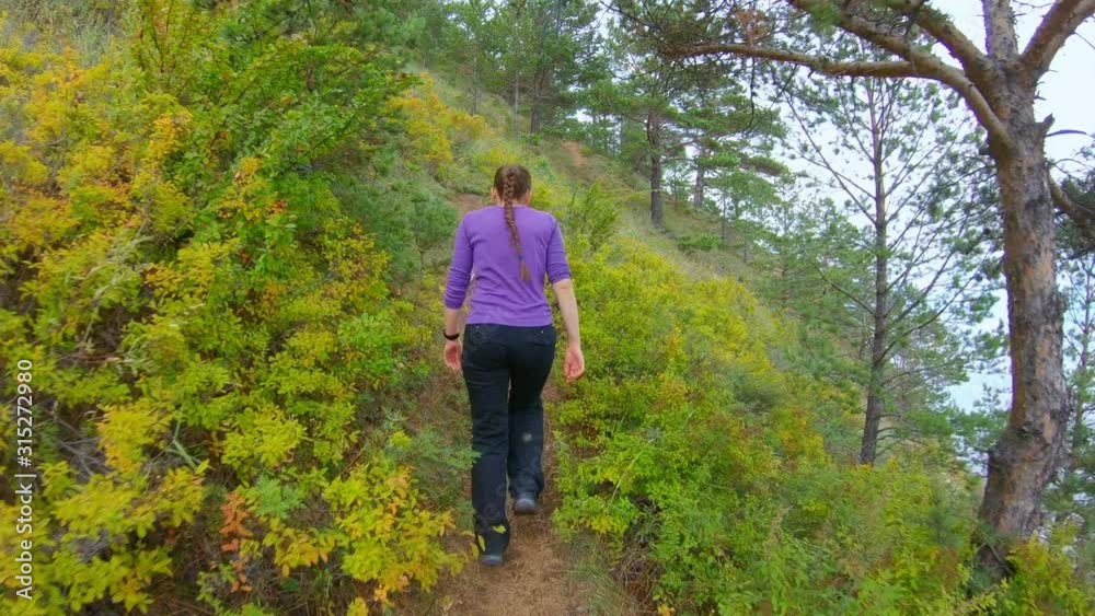 Girl climbs the path on the steep slope of the coast in the autumn. Slow motion, back view Girl climbs the path on the steep slope of the coast in the autumn. Slow motion, back view