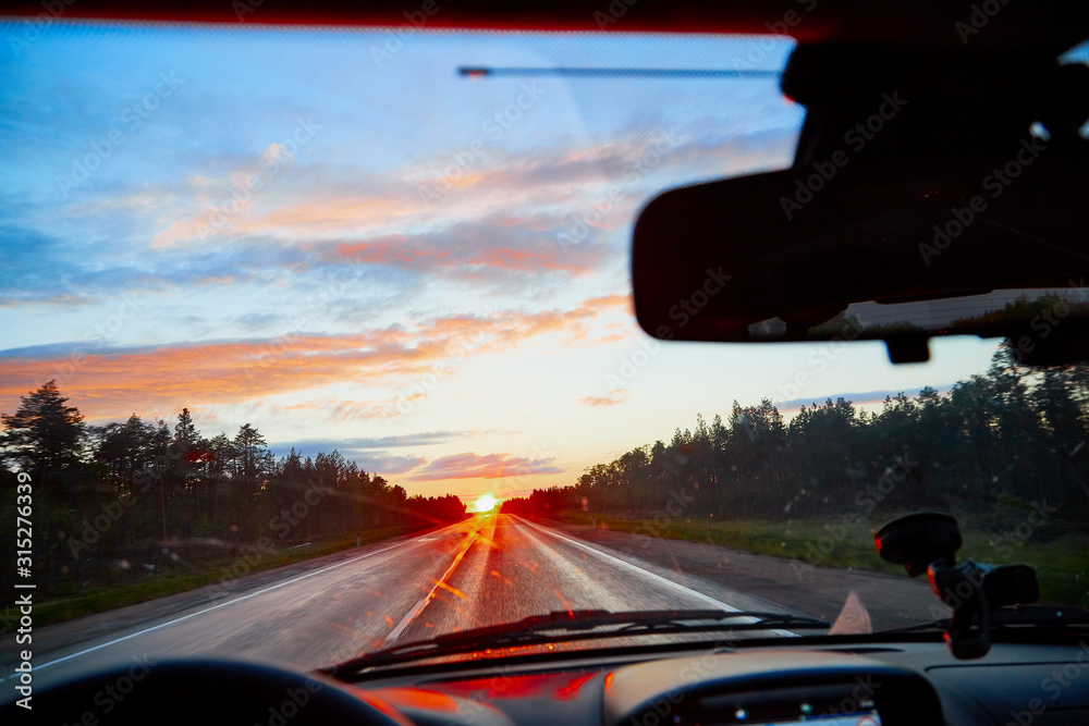 Red sunset view with shining sun from the car front window. Driving car during sunset concept. View on nature landscape and a road from car cabin Red sunset view with shining sun from the car front window. Driving car during sunset concept. View on nature landscape and a road from car cabin