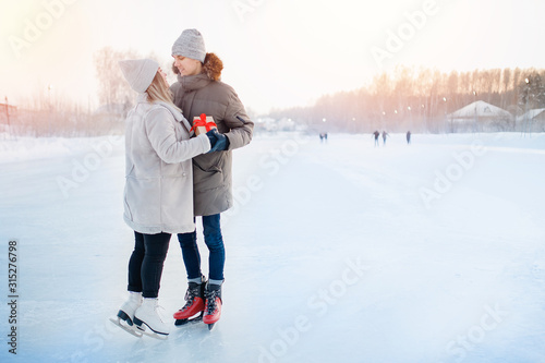 Man giving gift box girlfriend winter on ice rink, surprise romantic for Valentine Day or Christmas. Background snow sunset
