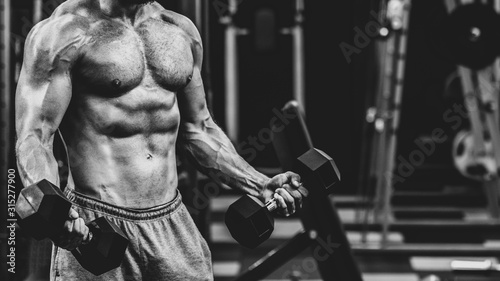 close up of Muscular athletic bodybuilder working hard in gym on dark background, dramatic black and white image © Denys Kurbatov