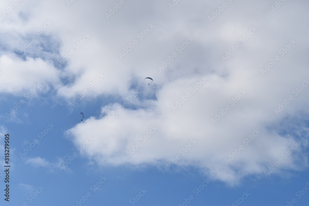 Paraglider in the wide blue sky with a white cloud in background