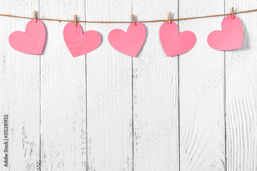 White painted wooden background with a garland of pink hearts. Natural rope and clothespins. Concept of recognition of love, romantic relationships, Valentine's day in grunge style. Copy space