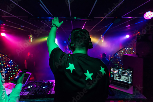 back of a male DJ with a raised hand in headphones at an electronic concert