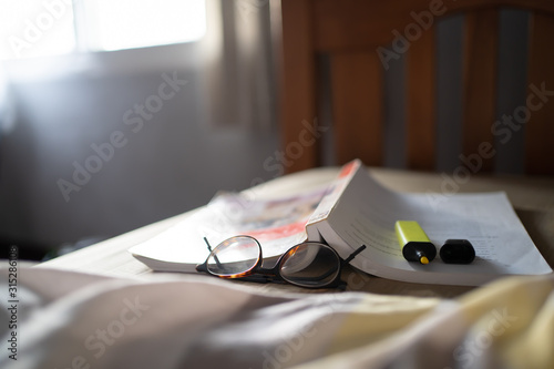 Textbook, Glasses and highlighter pen on the bed.