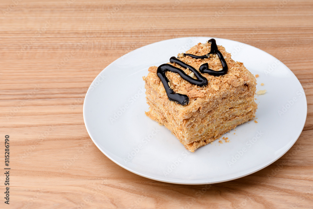 Piece of Napoleon cake served on white plate over light wooden table background. Traditional sweet dessert.