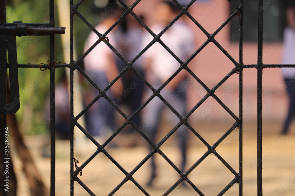 Focus On School Iron Metal Grill Gate With Students Playing In Playground in Blur Background Focus On School Iron Metal Grill Gate With Students Playing In Playground in Blur Background