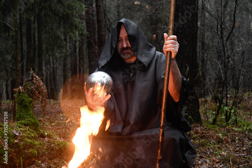 Slika na platnu A black-robed monk sits by a fire in the forest and looks into a divination ball