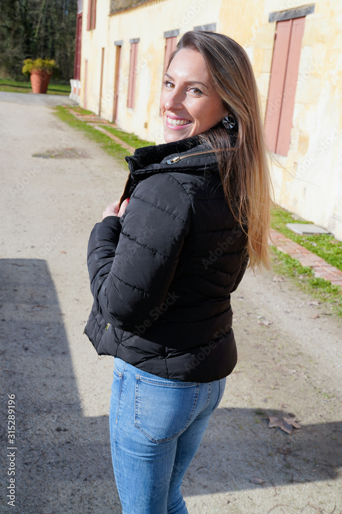 Young fashion slim woman blond in black jacket walking in city street rear behind view