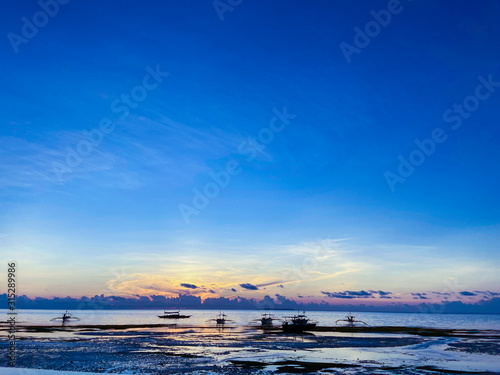 Beautiful  magical sunset  sunrise. Calm sea with boats on the background sky and clouds. Low tide on beach. Blue trend