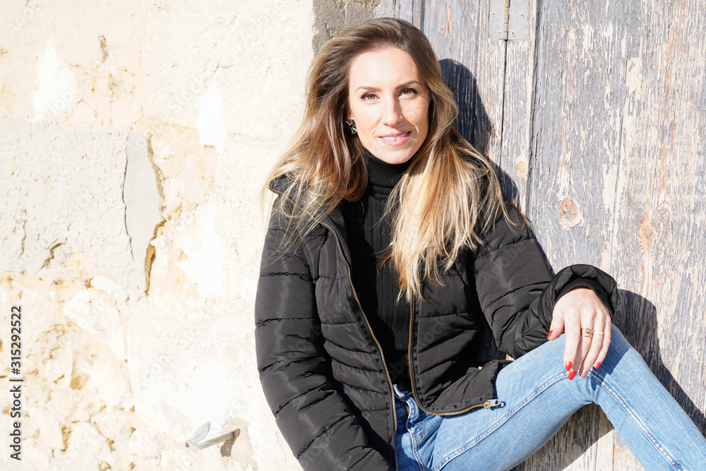 woman pretty blonde in black jacket leaning on wall sitting on street woman pretty blonde in black jacket leaning on wall sitting on street