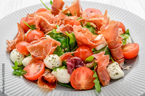 Salad with fresh vegetables with dried tomatoes, meat and mustard, mozzarella, prosciutto