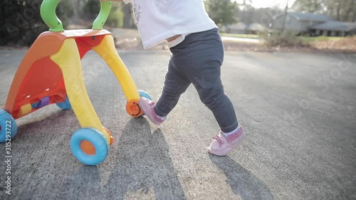One year old baby just learning how to walk, practicing first steps with a push toy walker.