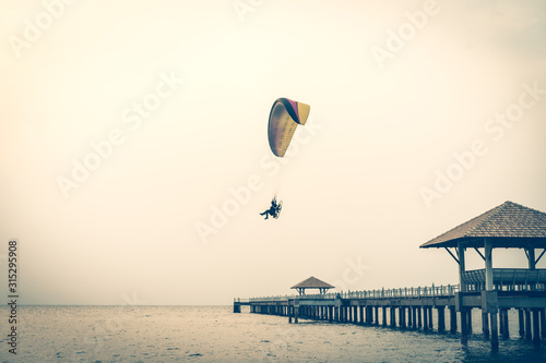 A man is flying with a powered parachute over the beach in Thailand.