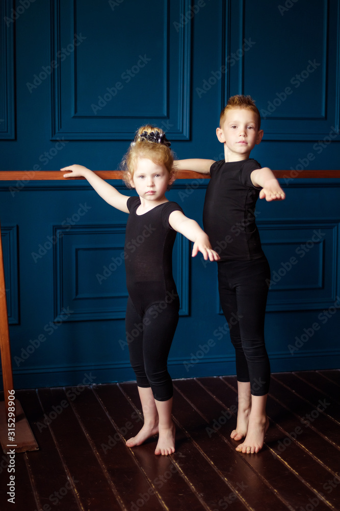 Obraz premium Portrait of little blonde curly ballerina and small boy dancer in black leotard practicing at ballet barre at dance studio. Kids hobby dancing. Active lifestyle in childhood. Brother and sister