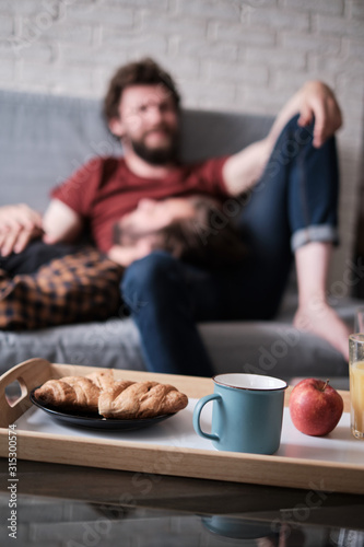 Food and glasses stand on the table with a gay couple on the background.