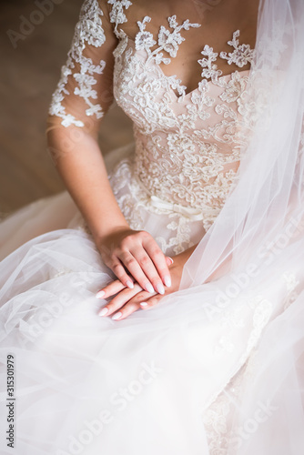Wedding morning of the bride. Hands close-up with a gold ring. Wedding manicure close-up. White veil in hand, against the background of a beautiful wedding dress