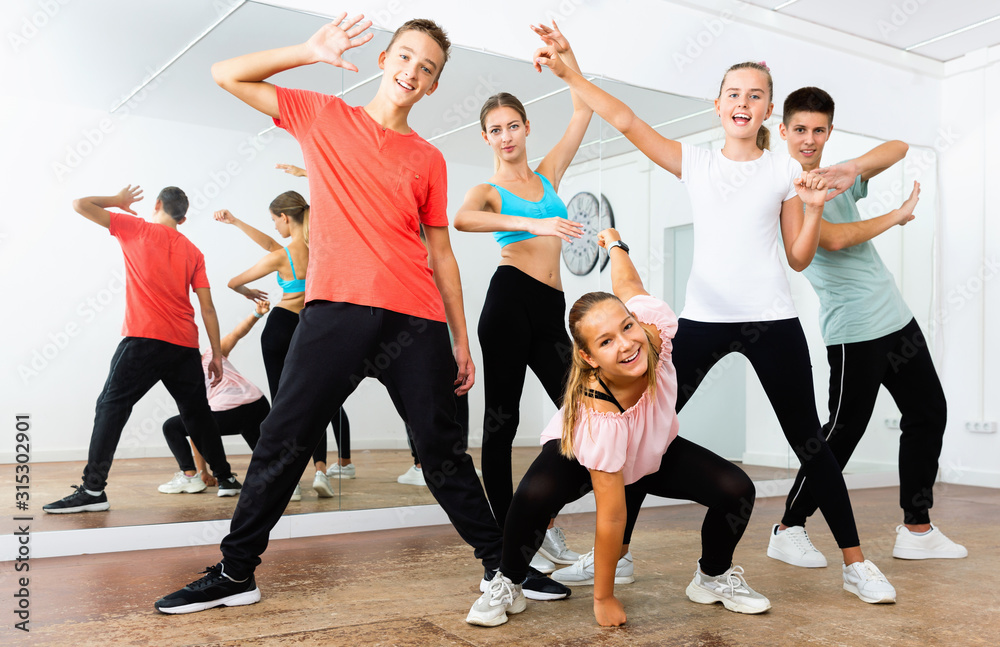 Cheerful teenage boys and girls having fun in choreography class, posing with female trainer