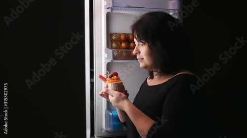 Woman night at the fridge eating a cake.Hunger,overeating,diet.
