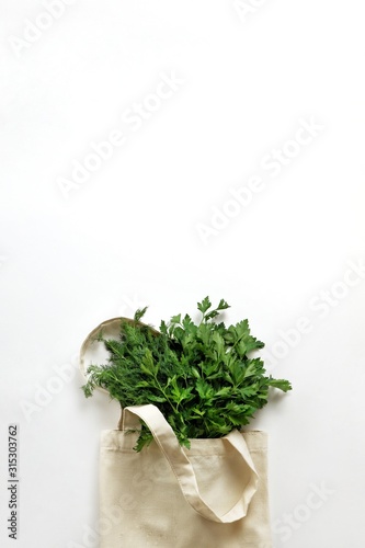A bunch of fresh organic greenery parsley and dill in a cotton reusable bag on a white background. Healthy food, organic products, eco friendly lifestyle, zero waste concept. Top view, copy space.