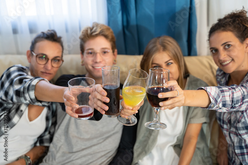 Hands of a group of young people with glasses toasting sitting on a sofa