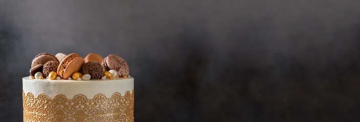 Confectionery, bakery banner. Festive cake decorated with chocolate candies and macaroons on dark background. Copy space, close up