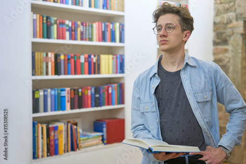 Thoughtful young man in a home library is thinking about the book he is reading, stone wall in the background.