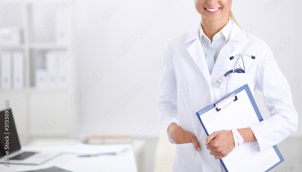 Smiling female doctor with a folder in uniform standing at hospital. Smiling female doctor Smiling female doctor with a folder in uniform standing at hospital. Smiling female doctor
