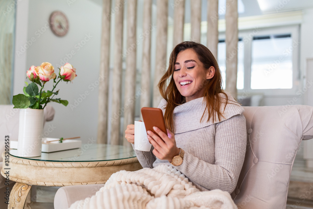 Pretty young woman sitting on sofa and enjoying first morning coffee in cozy apartment. Attractive young woman chatting with friends at social network while sitting on sofa at home and drinking coffee Pretty young woman sitting on sofa and enjoying first morning coffee in cozy apartment. Attractive young woman chatting with friends at social network while sitting on sofa at home and drinking coffee