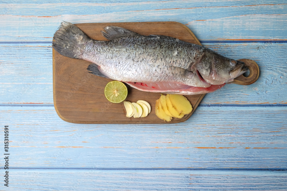 Barramundi or asian seabass fish with ginger,garlic,and key lime over the wooden cutting board. Barramundi or asian seabass fish with ginger,garlic,and key lime over the wooden cutting board.