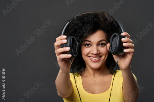 Smiling woman giving you headphones, studio shot